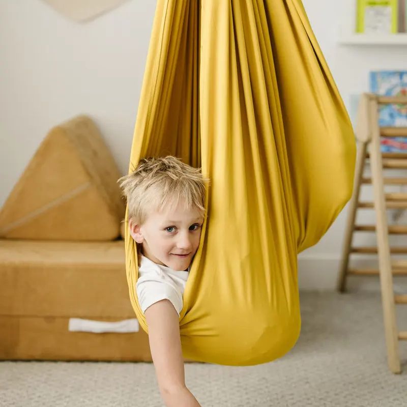 Criança explorando balanço sensorial dourado em ambiente interno